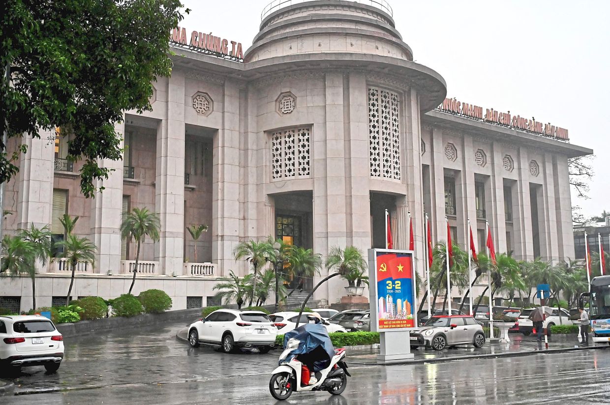 A woman rides a motorbike past the State Bank of Vietnam in Hanoi on February 25, 2025. (Photo by Nhac NGUYEN / AFP) 