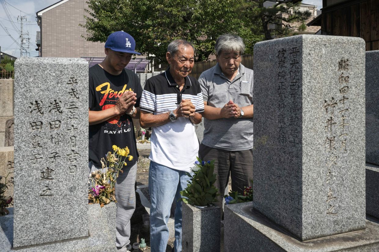 Jose Villafuerte (centre) praying with his son Avelino Villafuerte (left) and his Japanese half-brother Hiroyuki Takei (right) at the gravesite of their father Ginjiro Takei together for the first time, in the city of Takatsuki in Osaka prefecture. - AFP