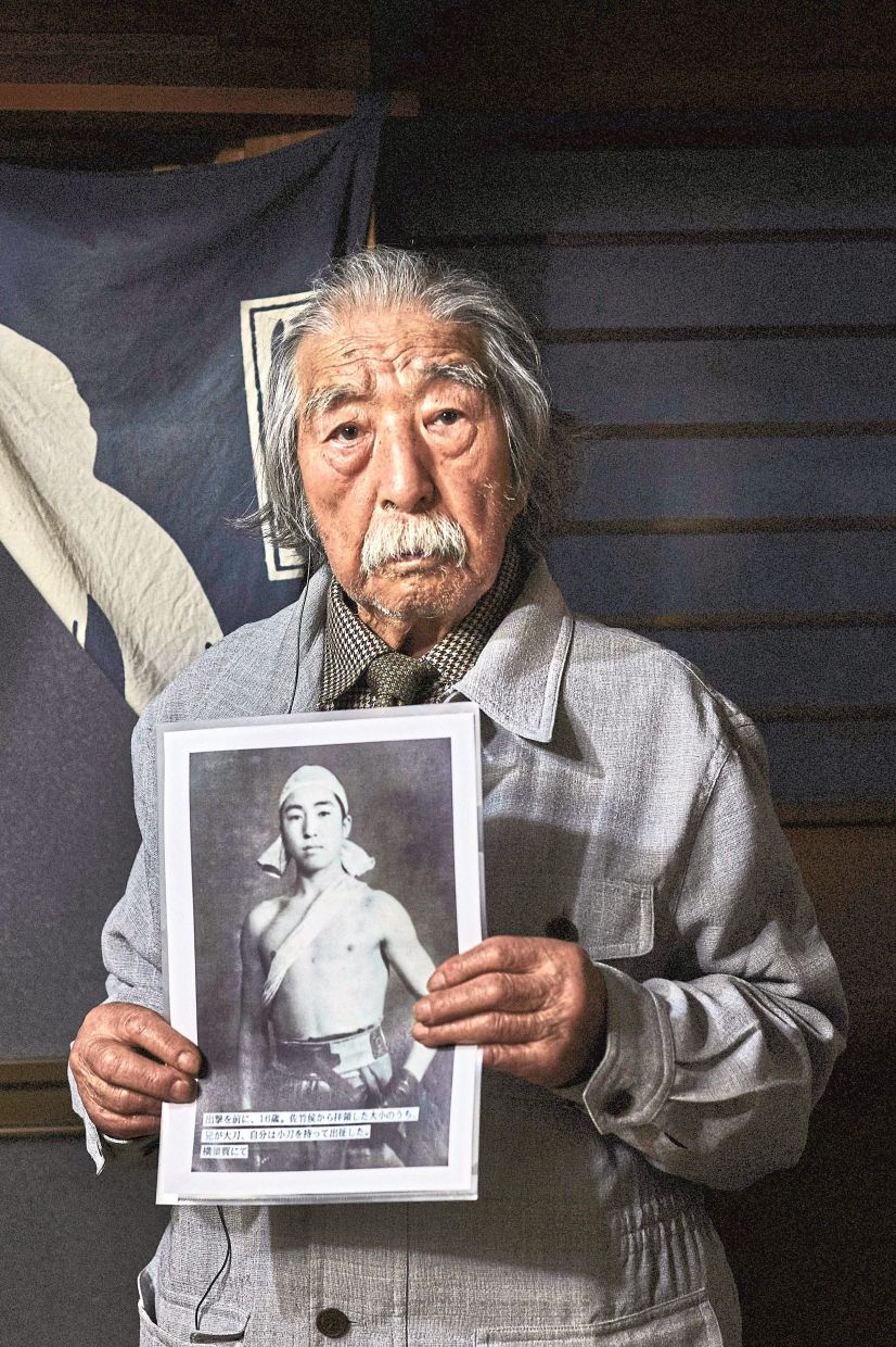 Suzuki, 96, holding a photograph of himself at age 16 before his deployment, at his home in Tokyo.