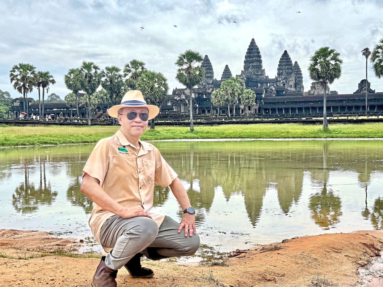 The author taking the chance to pose next to a pool of water showing a reflection of the temple. 