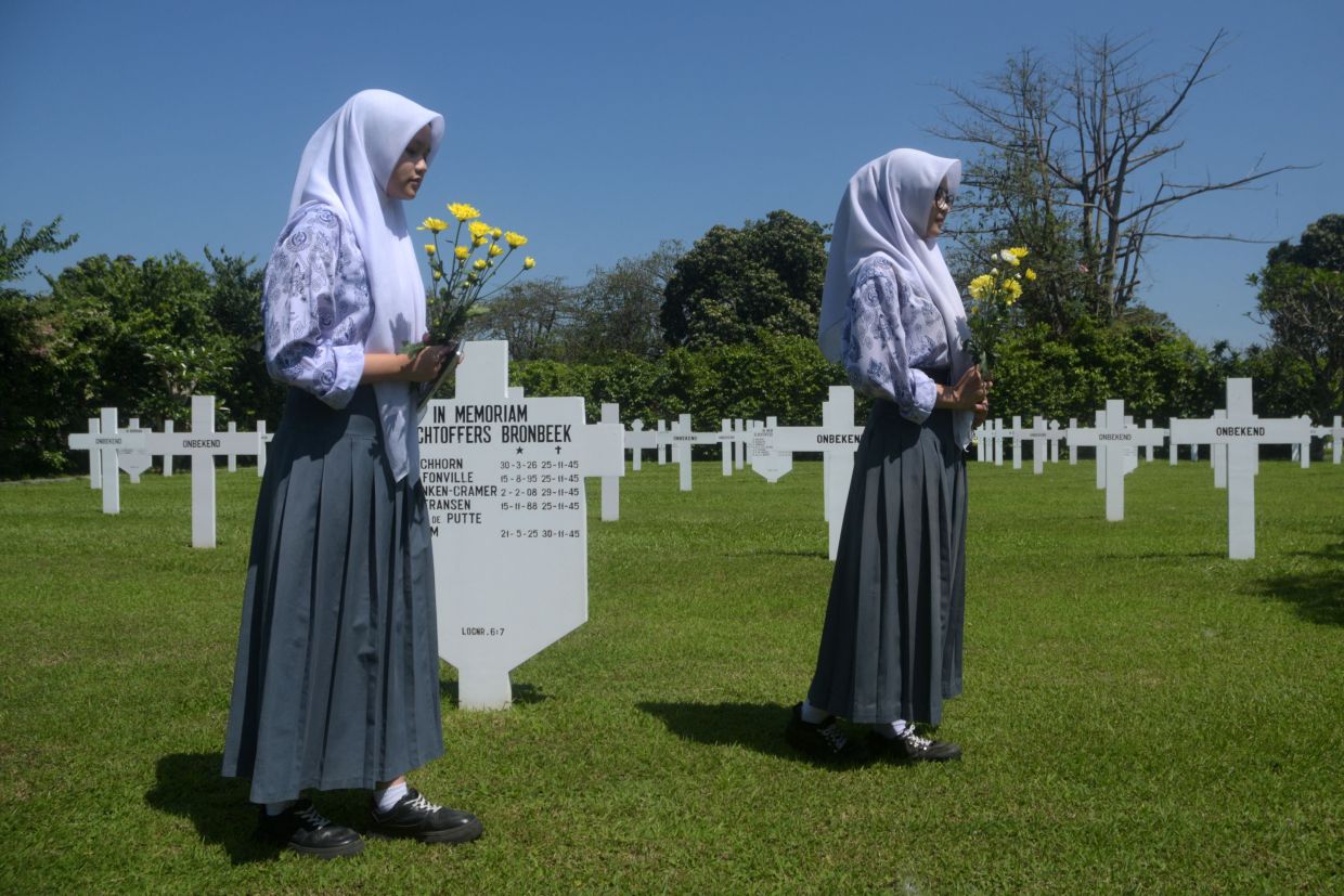 High school students hold flowers for a ceremony marking the 80th anniversary of the end of World War II, at the Ereveld Pandu cemetery where Dutch soldiers who died in the war are buried in Bandung, West Java, on Friday, August 15, 2025. -- Photo by TImur Matahari / AFP