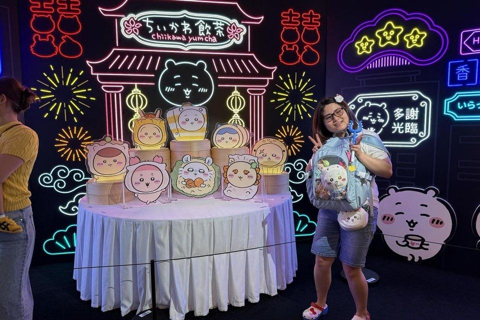 A fan poses with the dimsum display at the indoor zone of the Chiikawa Days exhibition in Tsim Sha Tsui. She is decked out in merchandise including two bags, hair clip, magic wand and T-shirt. - Photo: ST