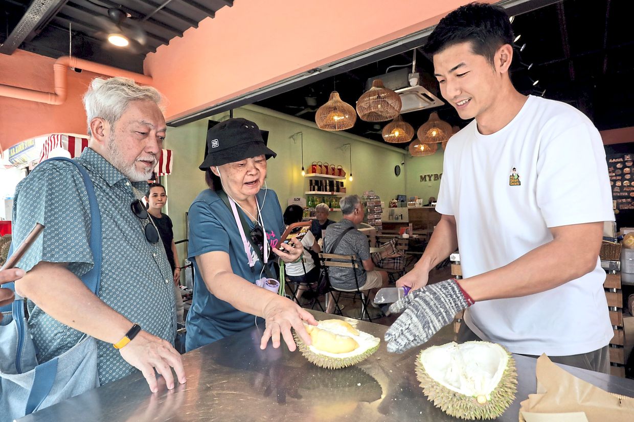 Choy and Foo (left) are Singaporean tourists who make the annual trip to Ang's durian store MyBolehBoleh every year in pursuit of good durian. — SAMUEL ONG/The Star