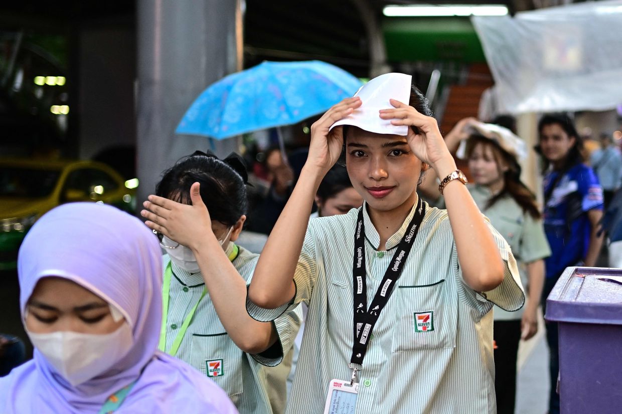 A woman covers her head with a sheet of paper as she walks along a street during a drizzle in Bangkok on Monday, August 18, 2025. -- Photo by MANAN VATSYAYANA / AFP