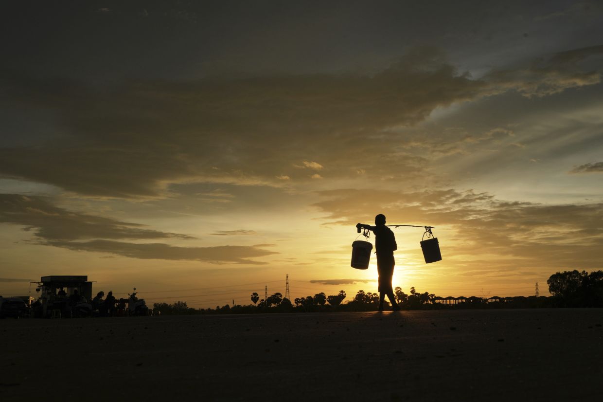 A man is silhouetted as he carries plastic containers while heading home outside Phnom Penh, Cambodia, Monday, Aug. 18, 2025. -- AP Photo/Heng Sinith