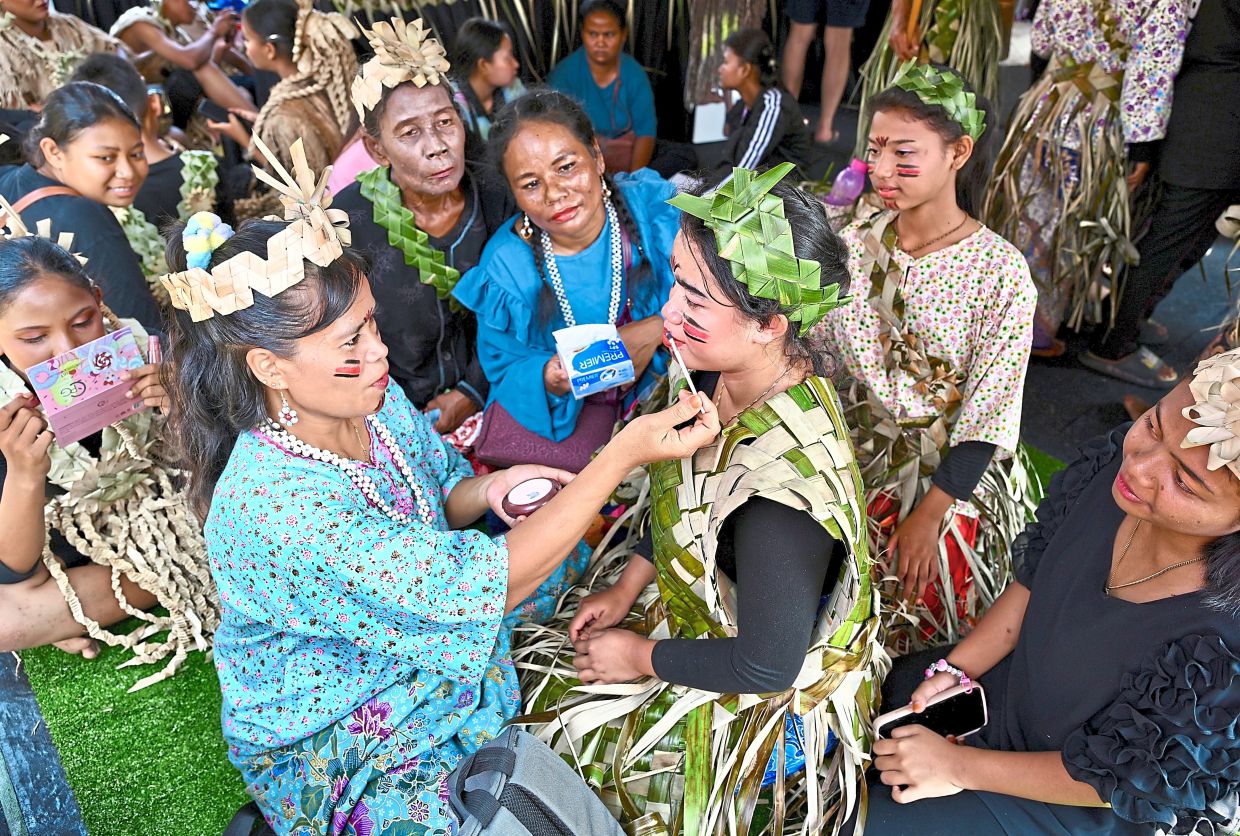 Temuan women adorning their faces with natural pigments and symbolic patterns while preparing for a cultural dance.