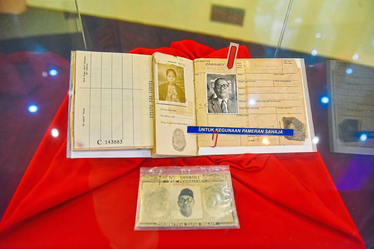 The identity card of Malaysia’s first prime minister Tunku Abdul Rahman Putra Al-Haj on display at the NRD museum. (Right) Badrul Hisham showing old identity cards.
