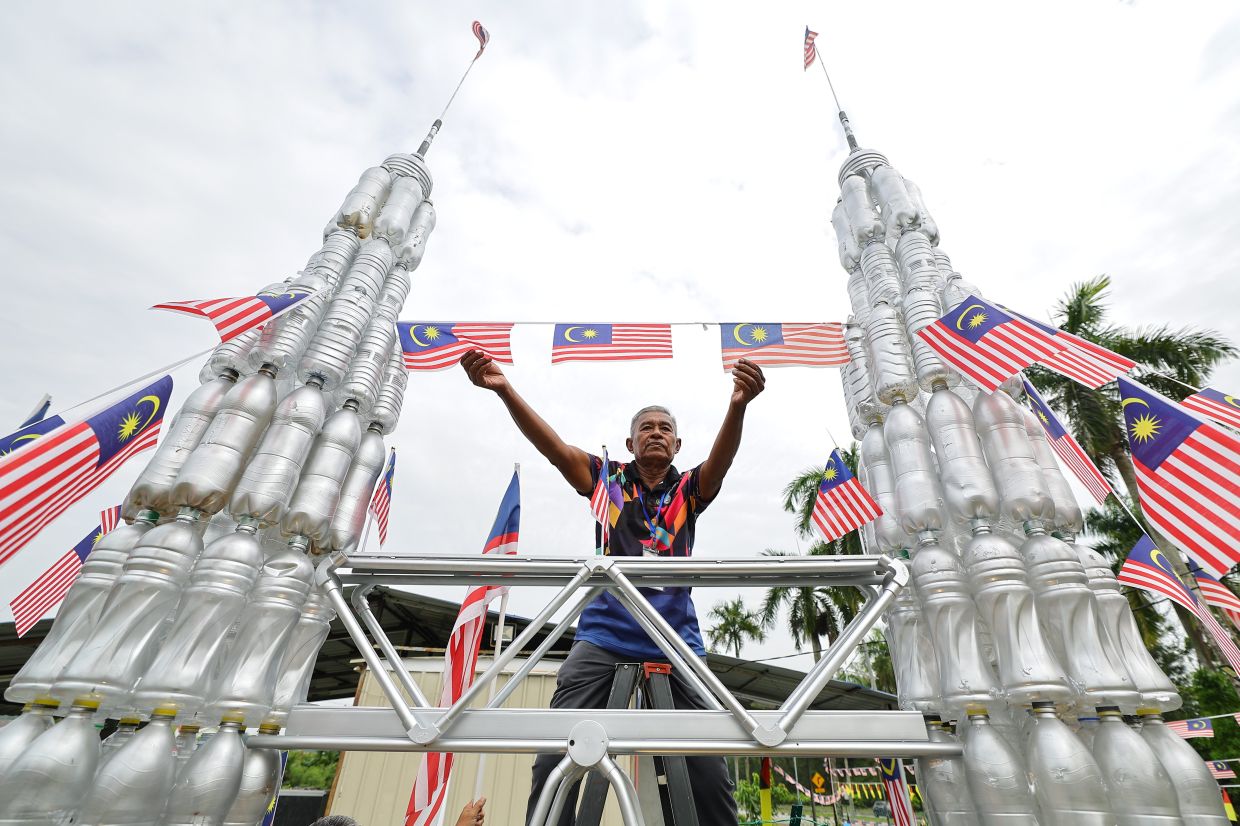 Taman Pinggiran Senawang KRT member Amran Ahmad is seen putting on the finishing touches on a national landmark replica - the KLCC towers - as part of the National Month decorations, using 500 recycled bottles, PVC pipes and several other materials.