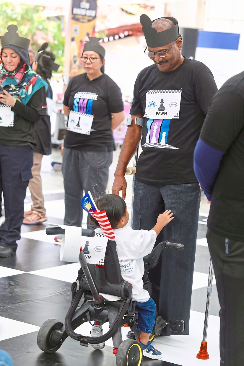 Isaiah standing in a white square, facing a young SMA patient in the chess match.