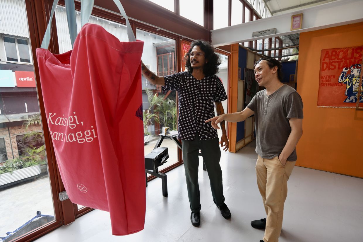 Sanan showing a visitor his artwork 'Kais Pagi, Makan Maggi' (2025), a screen print on handmade oversized tote bag. Photo: The Star/Low Lay Phon