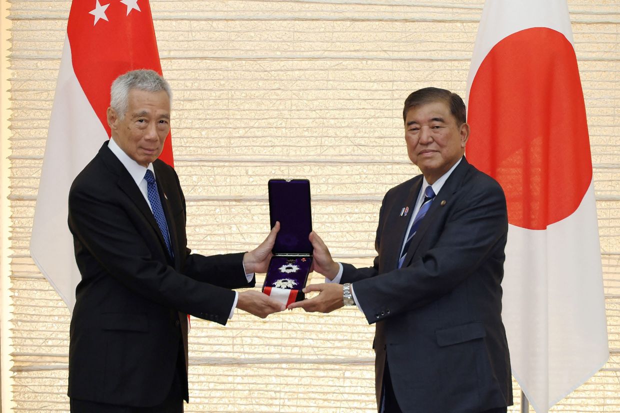 Japan's Prime Minister Shigeru Ishiba (right) presents the Grand Cordon of the Order of the Rising Sun to Singapore's Senior Minister Lee Hsien Loong during a ceremony at the prime minister's office in Tokyo on Monday, August 25, 2025. -- Photo by JIJI Press / AFP