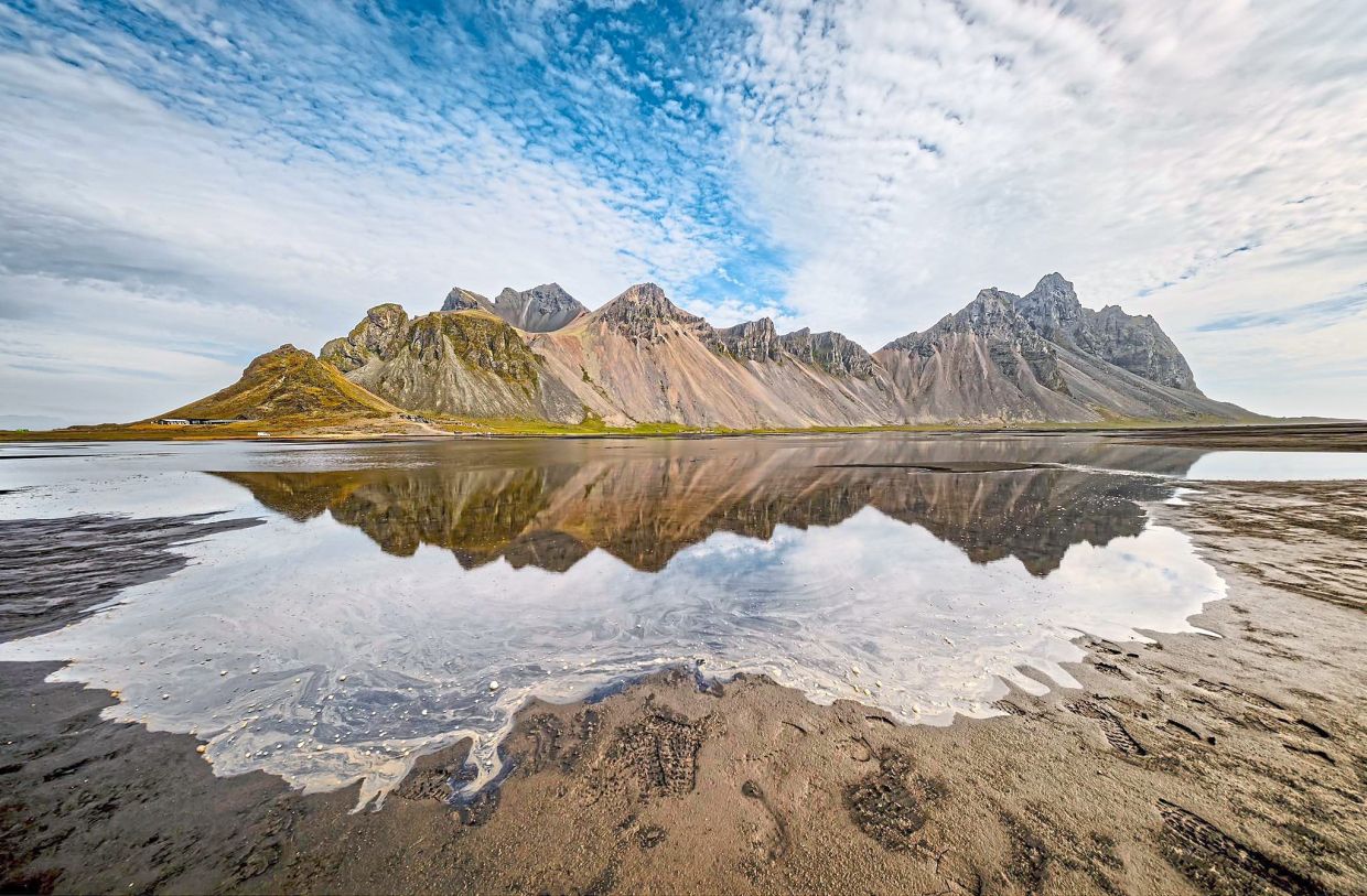 The jagged peaks of Vestrahorn mirrored in a black-sand lagoon, one of Iceland’s most dramatic coastal vistas.