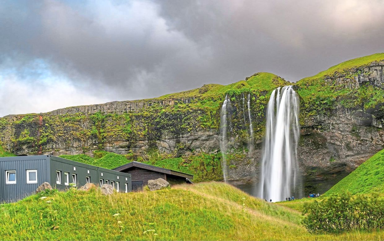 Seljalandsfoss, one of Iceland’s most recognisable waterfalls, cascades beside a quiet farmhouse beneath brooding skies.