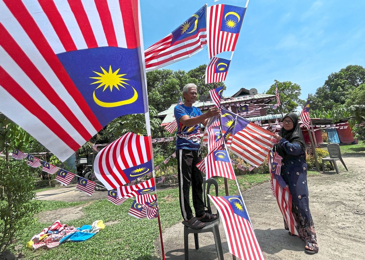 Former army man Abd Hamid Hussin getting help from wife Juriah Samat to decorate their house and yard at Kampung Titi Teras in Balik Pulau, Penang, with 1,000 pieces of Jalur Gemilang.