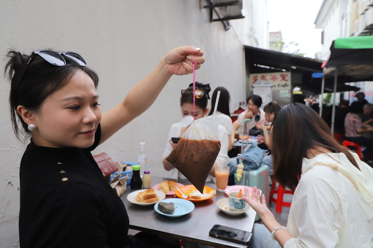 Novia Lin, 29, from China having coffee and breakfast in Toh Soon Cafe is located at a back lane along Campbell Street in Penang. — LIM BENG TATT/The Star