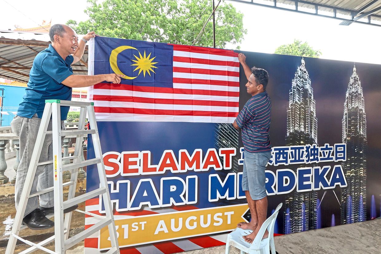 Wang (left) putting up the Malaysian flag at the multipurpose hall in Kampung Baru Plentong for their National Day celebration.