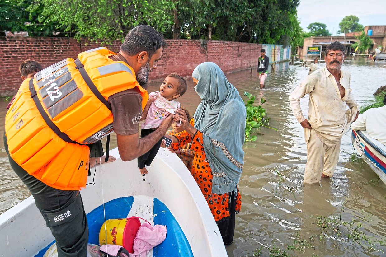 A rescue worker helping a family board a boat during evacuations in flood-hit Dhoop Sarhi village, Kasur district, Pakistan.— AFP/AP/Reuters