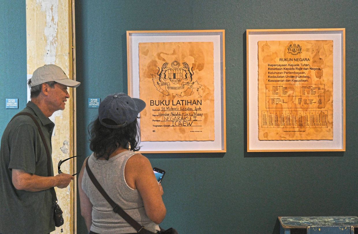 Visitors take a closer look at Arikwibowo Amril’s 'Buku Latihan Sim Kia Miang' - a work that taps into the nostalgia of school days - at the 'Negaraku II' exhibition at Hin Bus Depot in George Town. Photo: Bernama