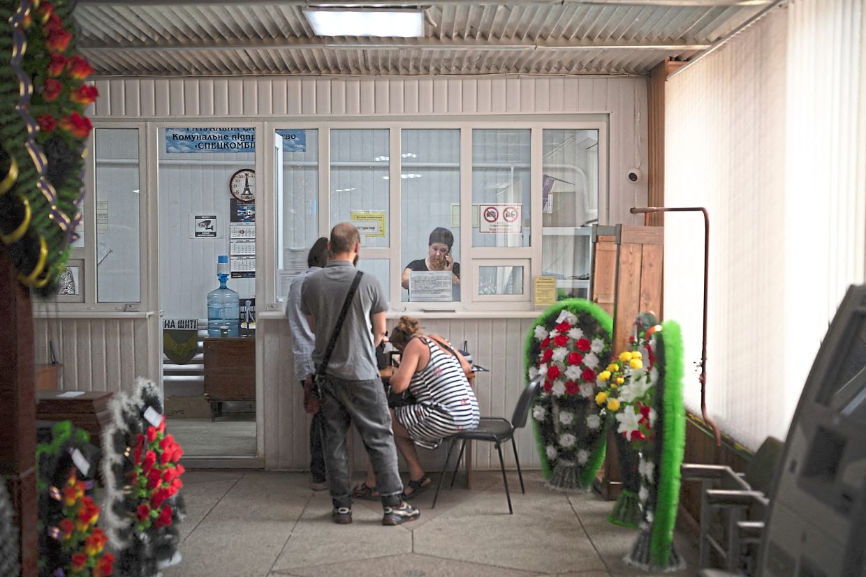 Ostapenko (right) seen behind her glass window, preparing funeral arrangements for a family whose son was killed on the front lines.