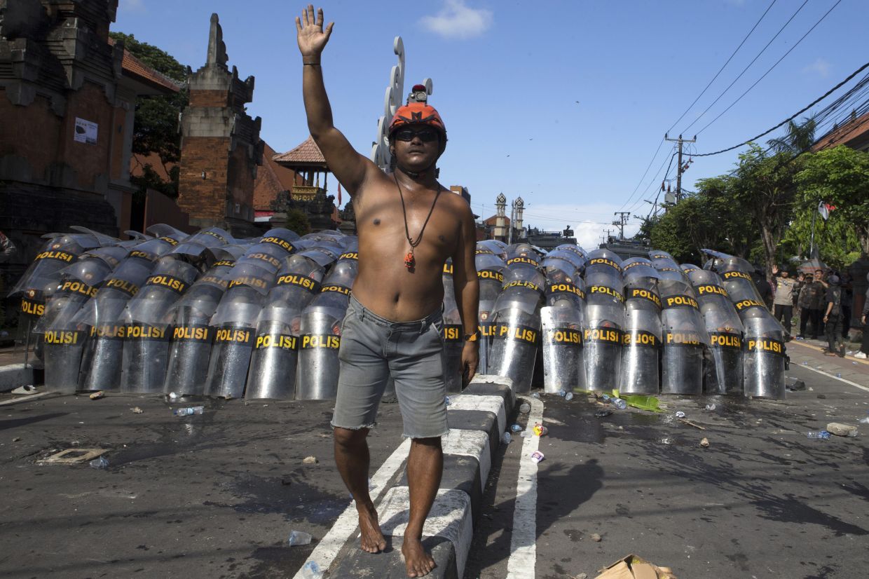 A man raises his hand to calm down protesters as police officers take a defensive position during a protest against lavish lawmakers' allowance, in Denpasar, Bali, Indonesia, Saturday, Aug. 30, 2025. -- AP Photo/Firdia Lisnawati