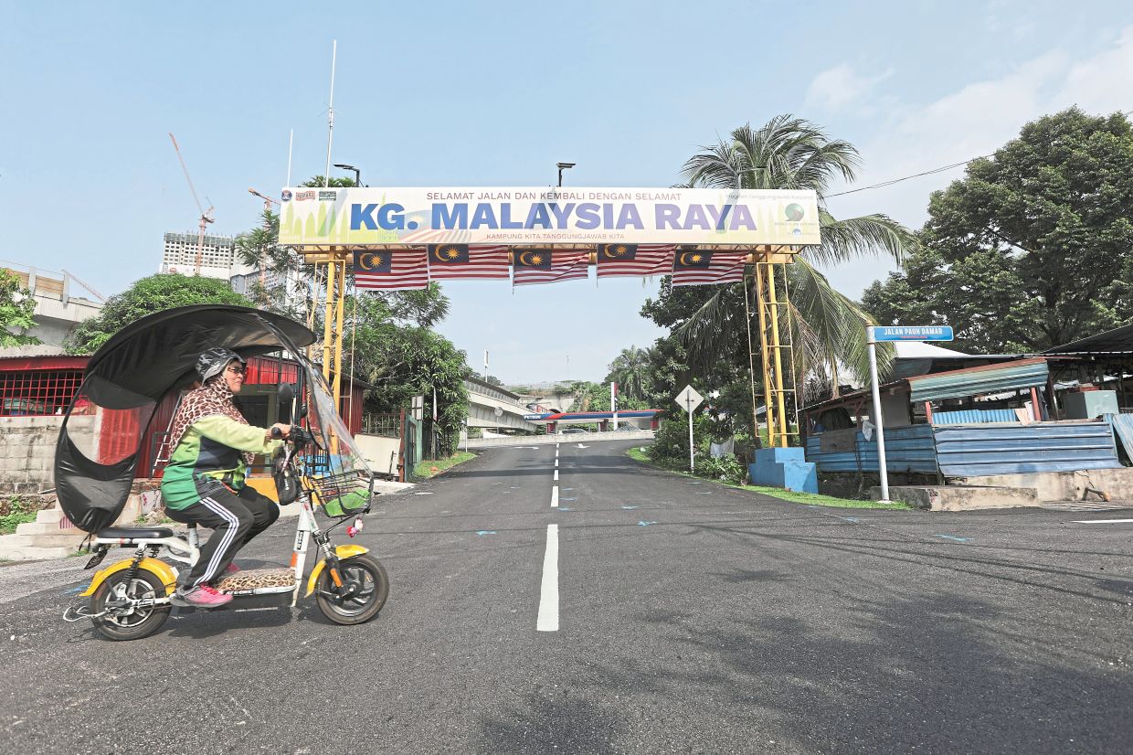 Sharimah riding her electric bicycle past the Kampung Malaysia Raya welcome arch in Sungai Besi.