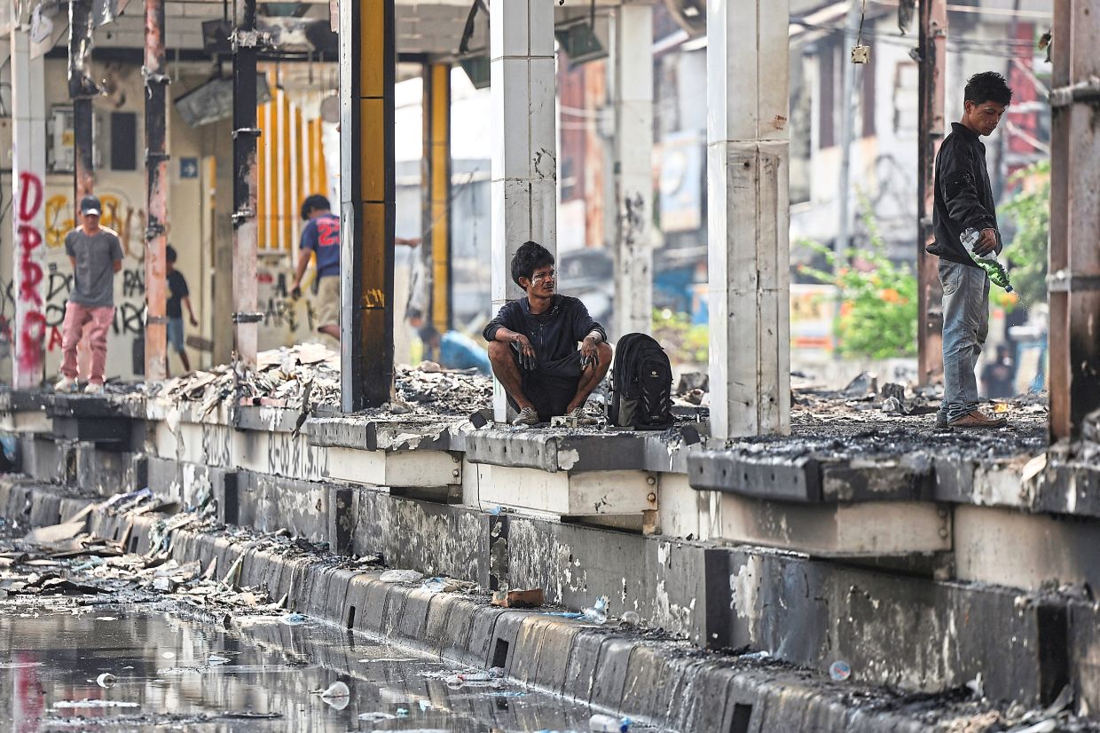 A man squatting at a bus stop burnt during a protest in Jakarta.