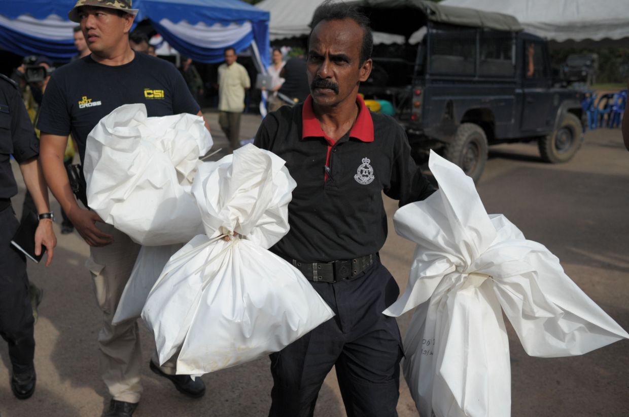 A Malaysian policeman carrying human skeletal remains inside plastic bags exhumed from hidden graves discovered near the Malaysia-Thailand border in Wang Kelian, Perlis, in 2015. AFP