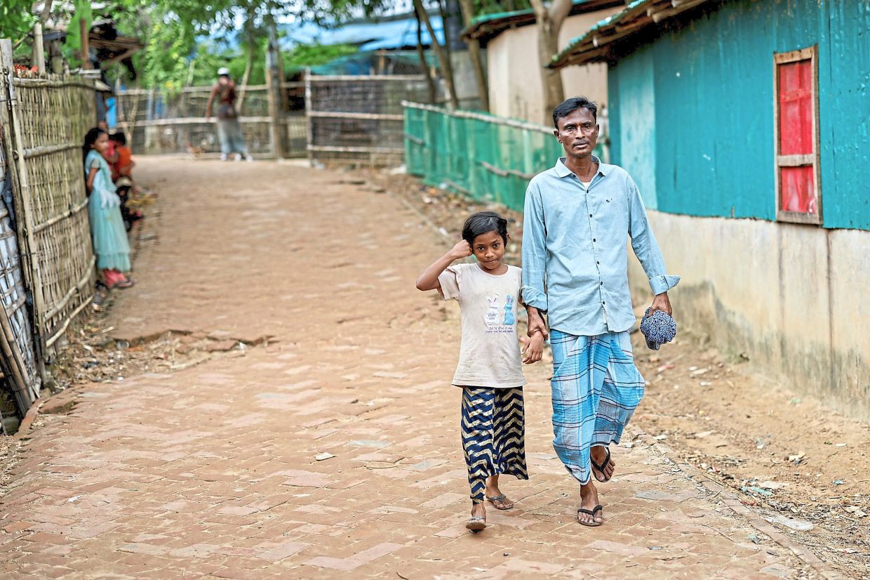 Faruq holding the hand of his nine-year-old daughter Nahima Bibi as they walk along the refugee camp.