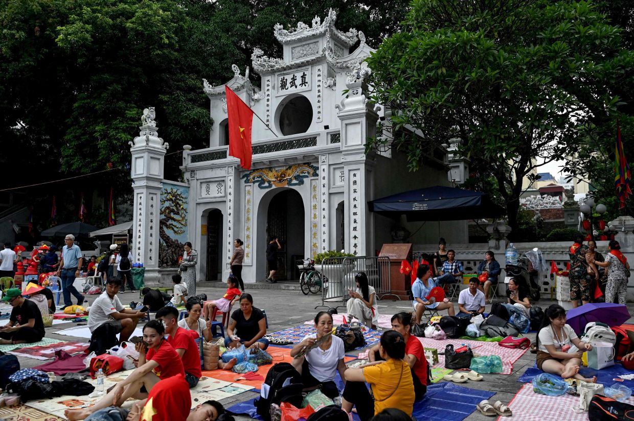 People wait on the sidewalk in front of Quan Thanh Temple, a day before Vietnam's National Day parade, in Hanoi on Monday, September 1, 2025. -- Photo by Nhac NGUYEN / AFP