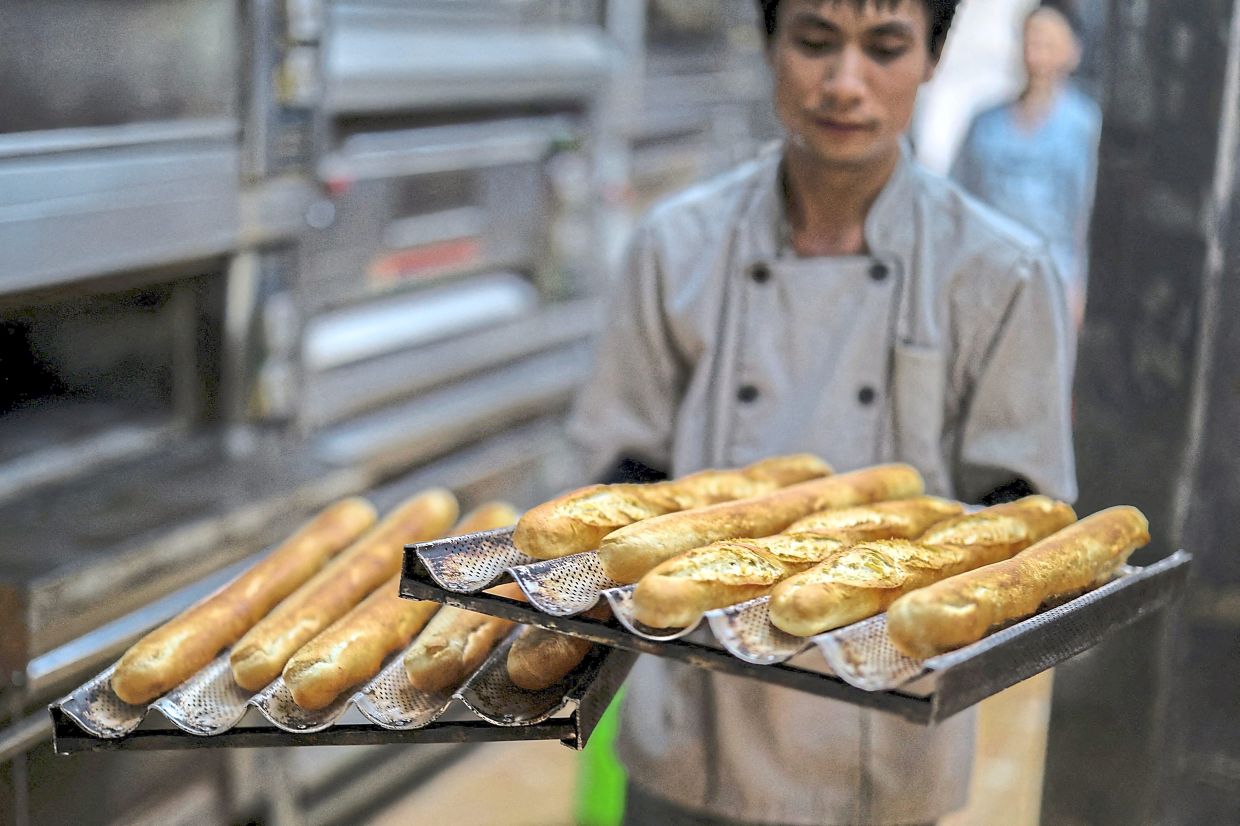 A baker holds up trays of baguettes at the Hoan Boulangerie bakery shop in Hanoi, Vietnam, August 30, 2025. REUTERS/Athit Perawongmetha