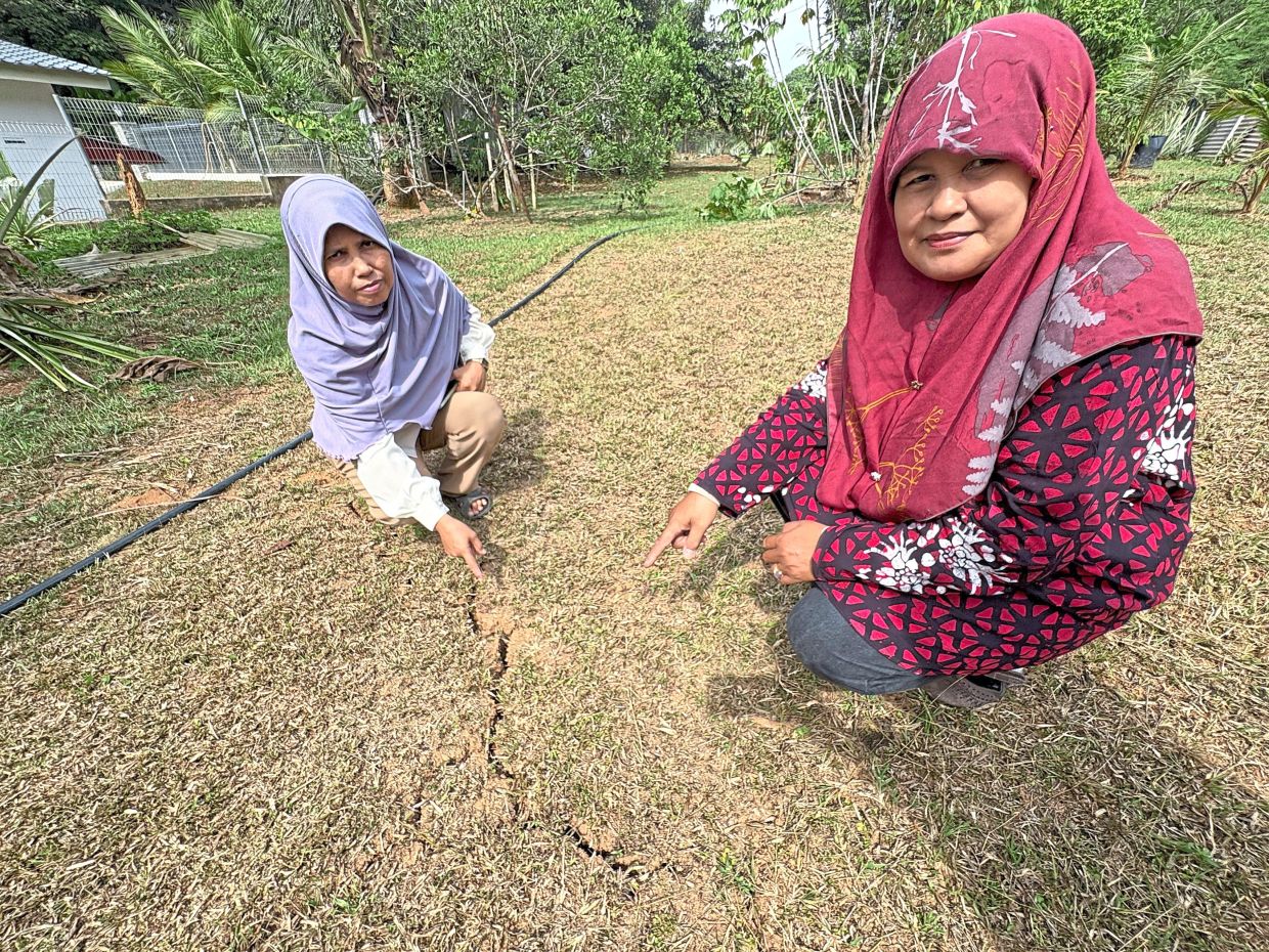 Signs of damage: Residents Ramlah Ishak (left) and her sister Umi Kalsom Ishak showing significant soil cracks in the garden area behind their house, believed to have been caused by tremors from an earthquake. — Bernama