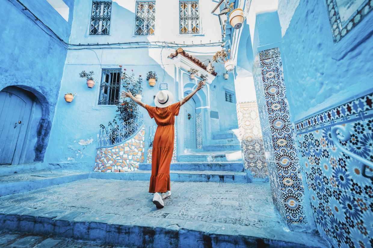 A traveller joyfully admiring the iconic blue-washed streets of Chefchaouen in Morocco.
