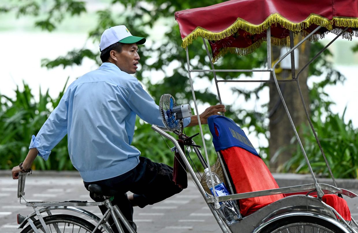 A rickshaw driver uses a portable electric fan to cool down from the heat as he waits for passengers in Hanoi on Monday, September 8, 2025. -- Photo by Nhac NGUYEN / AFP