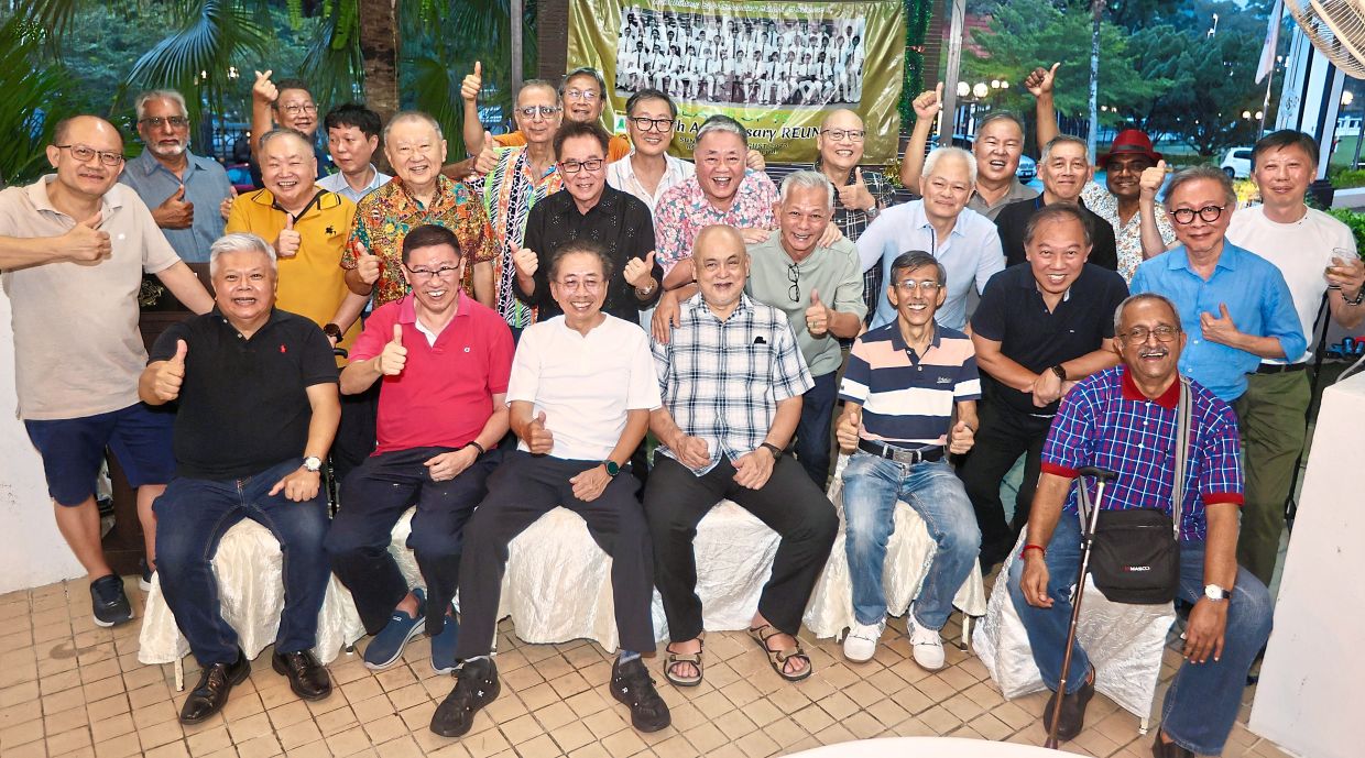 The old boys beaming as they pose for a group shot reminiscent of their class picture (in the background) five decades ago.