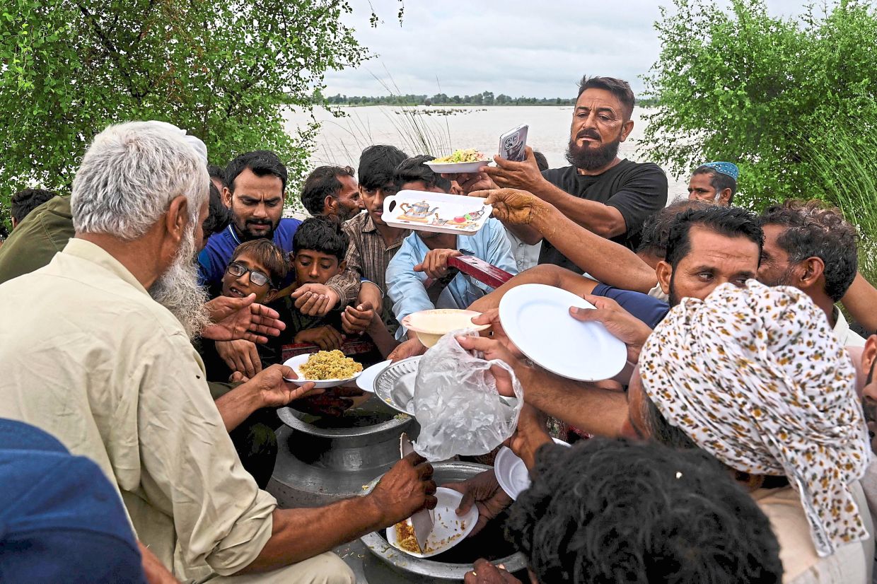 Keeping hunger at bay: Flood-affected victims receiving food aid at a makeshift relief camp in Kasur district. — AFP