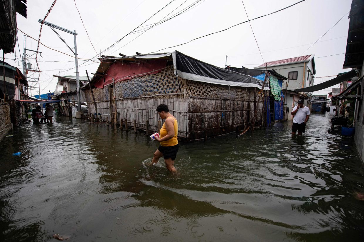 Residents wading through a flooded street on Isla Pugad in Hagonoy town. - AFP