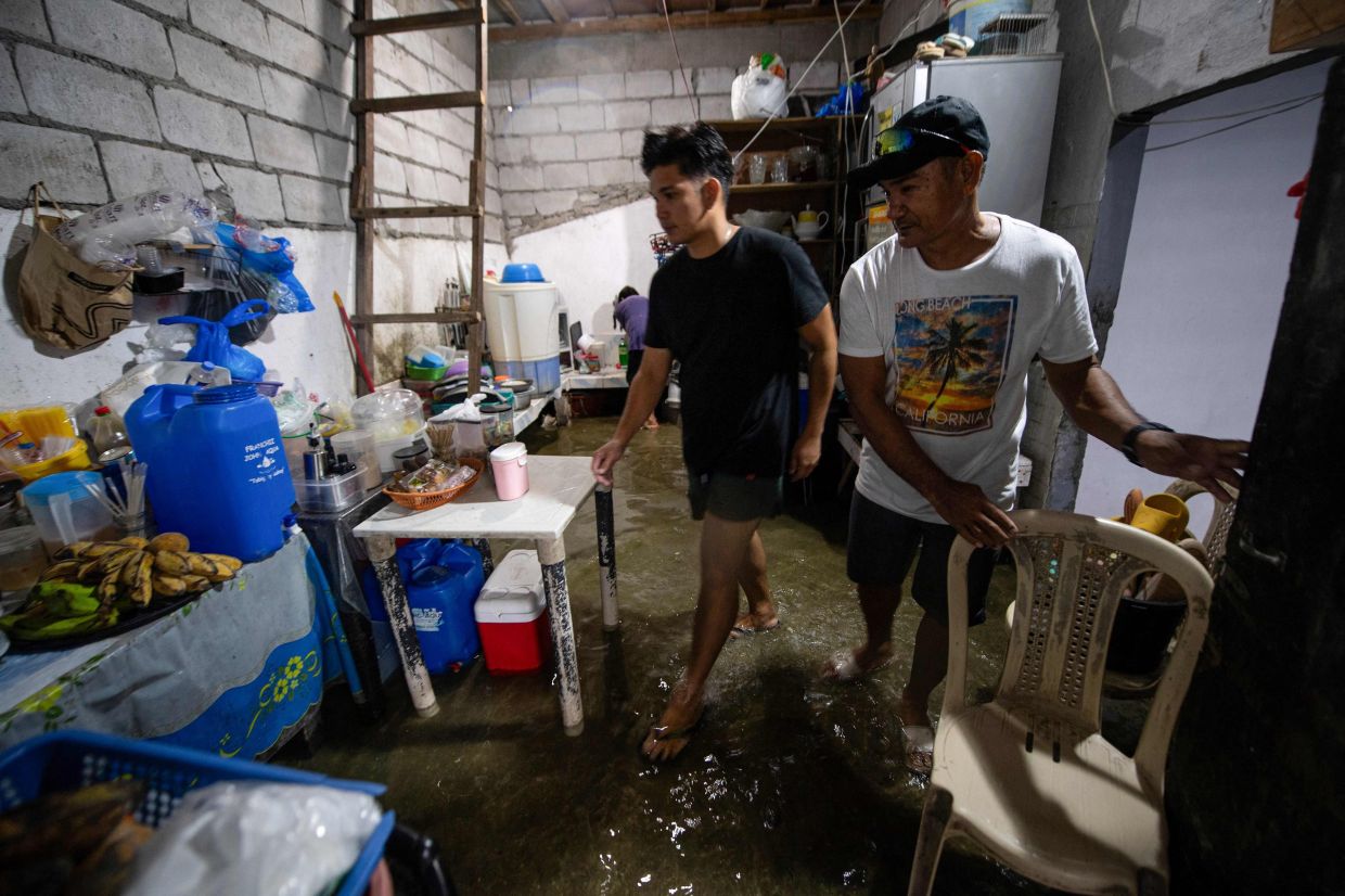 Raymart Tamayo (right) and his son Rodolfo (centre) walking in the kitchen of their flooded house on Isla Pugad. - AFP