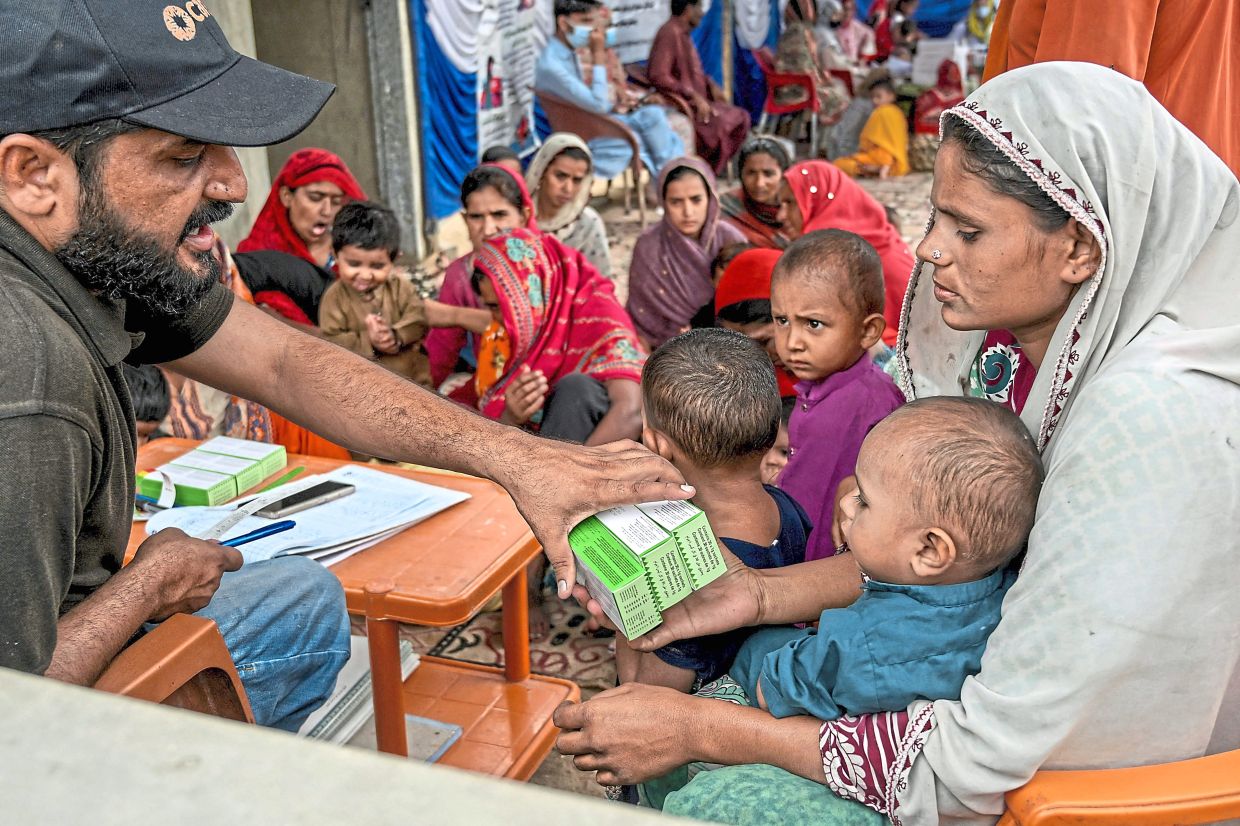 Sharing aid:A health worker (left) giving medicines after checking on children during a Unicef nutrition programme at Fateh Muhammad Soomro village.— AFP