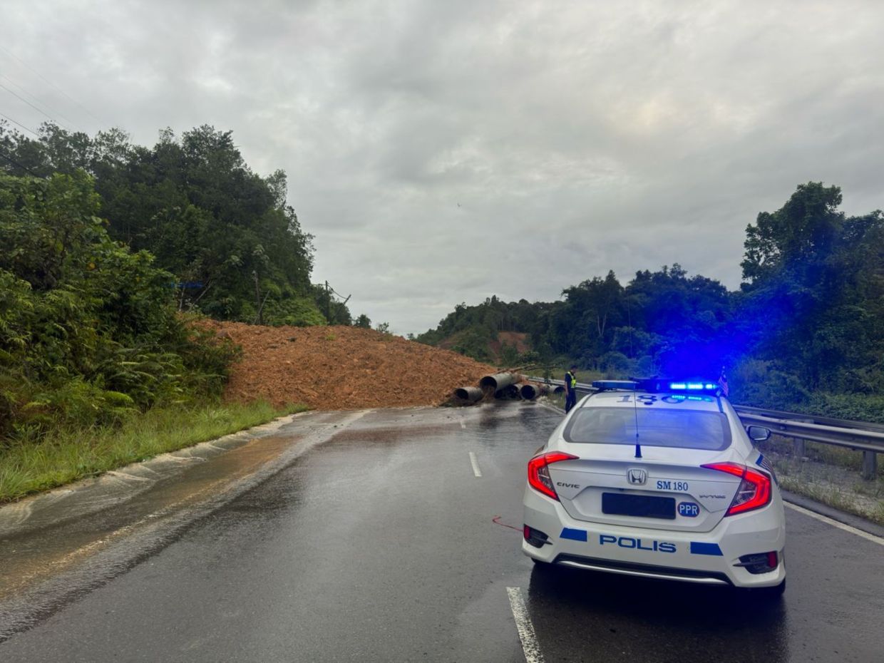 A patrol police checking on the landslide that covered part of the slope along Jalan Donggongon–Papar Spurs, cutting off access between Papar and Kota Kinabalu.