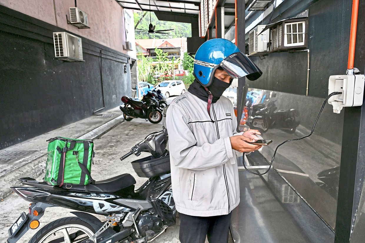 Delivery rider Farhan using a charger at the Riders Pit Stop to charge his handphone, which is important for him in finding locations to deliver items collected.