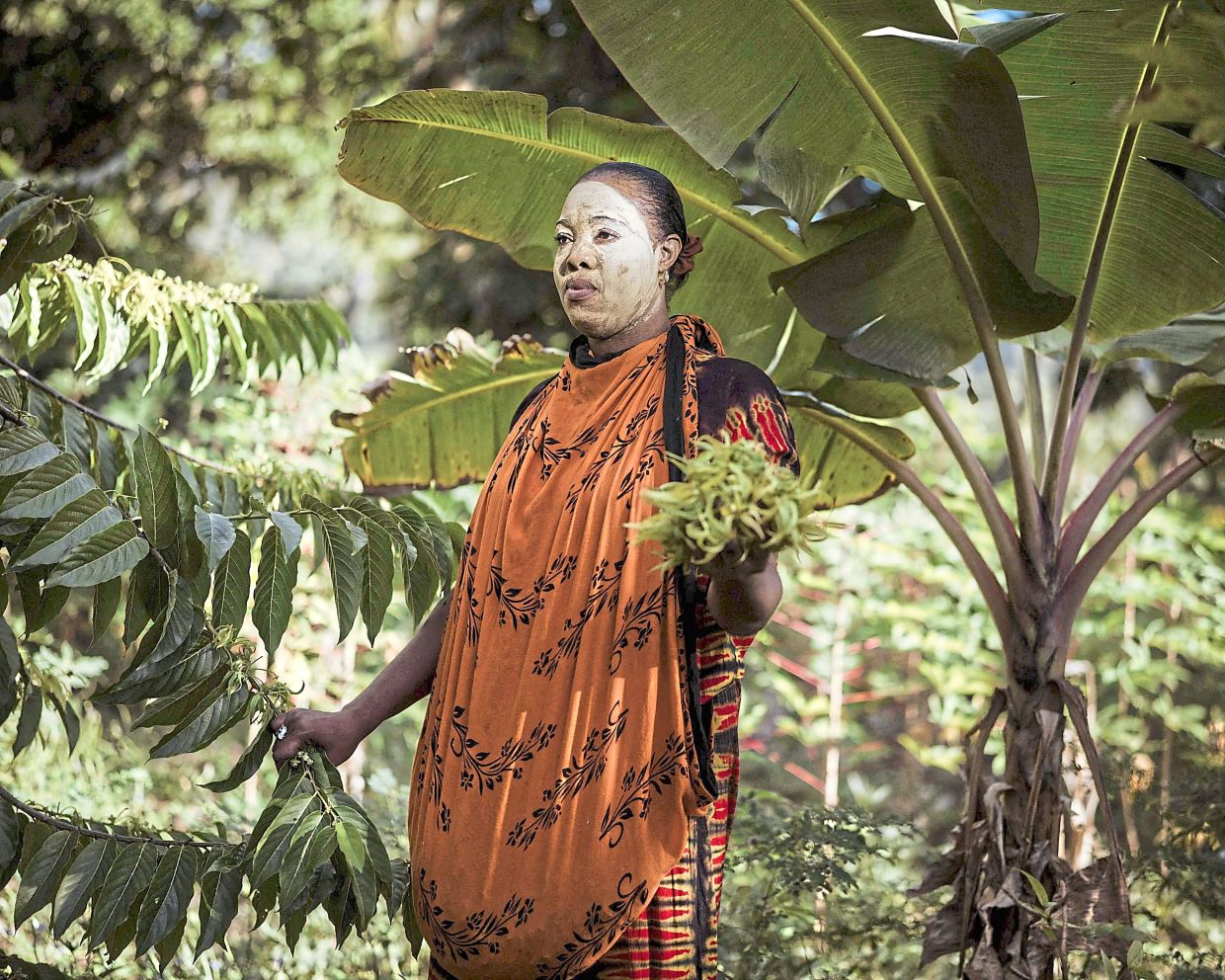 Sitti Fatima Mohamed, her face covered with a traditional msindanu mask (obtained by rubbing sandalwood on coral), poses for a portrait in a ylang-ylang flower field where she works as a labourer in Bambao Mtsanga. 