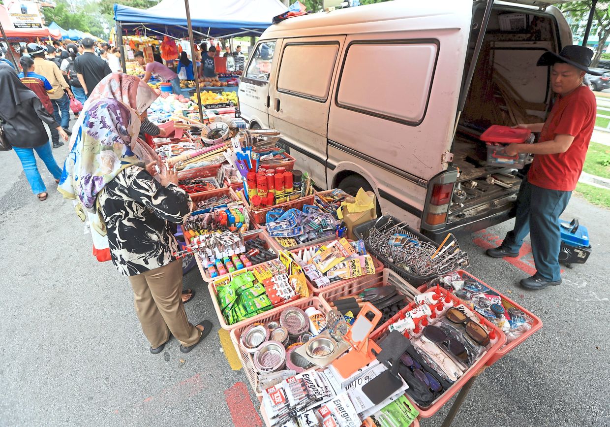 A vendor transferring household goods, tools and DIY items from a van for display on makeshift tabletops.