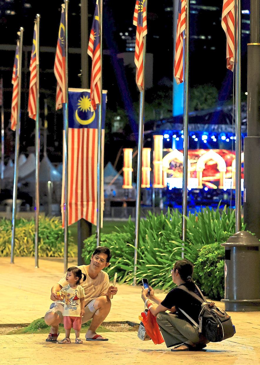 Under the lights of Dataran Merdeka, one family snaps shots of their child while another (pic, below) kicks back with snacks and stories. — Photos: CHAN TAK KONG/The Star