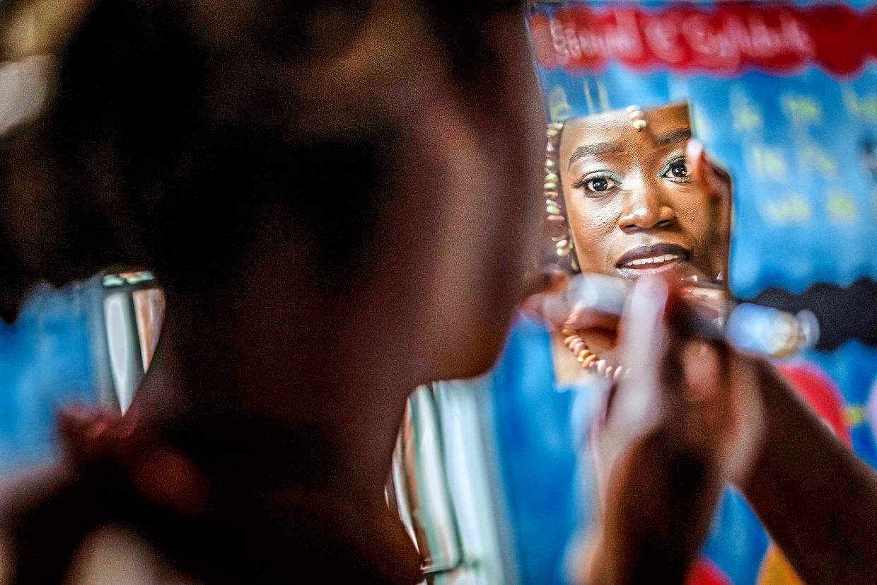 A participant in Mr and Ms Kibera 2025, held to mark International Youth Day, fixes her makeup during a break.