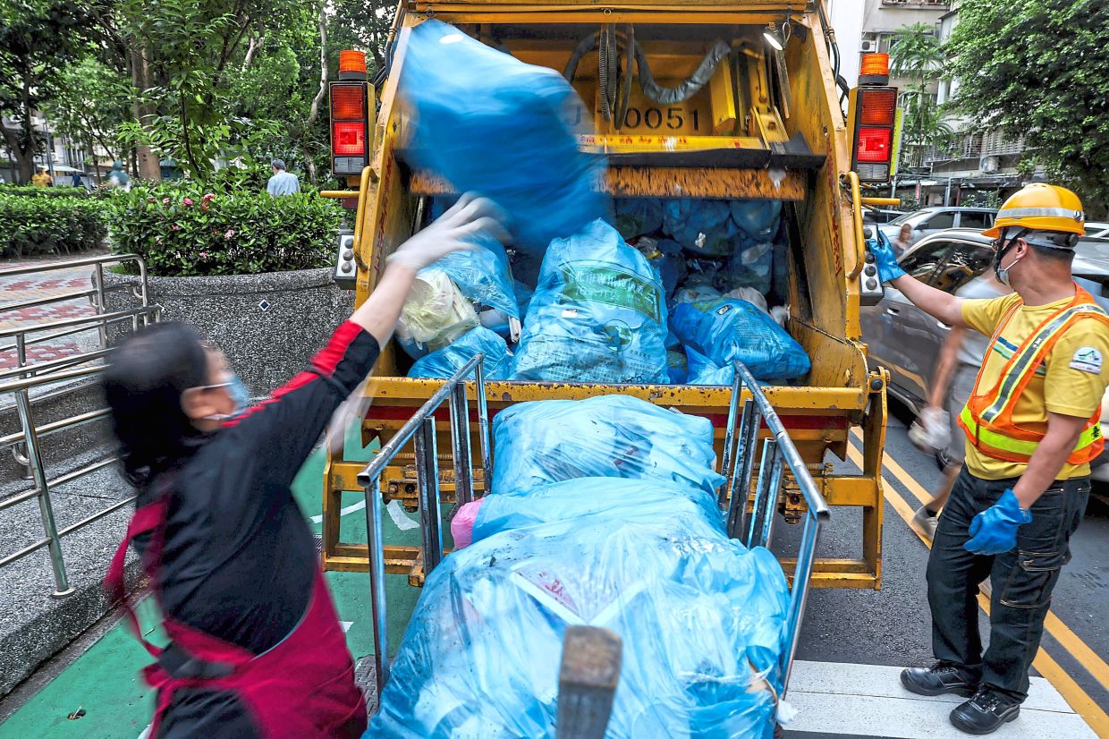 Taiwanese residents wait on a footpath as a garbage truck pulls up.