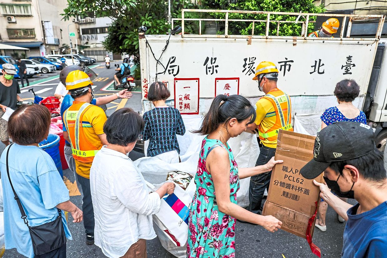 Residents folding cardboard boxes for recycling next to a collection truck.