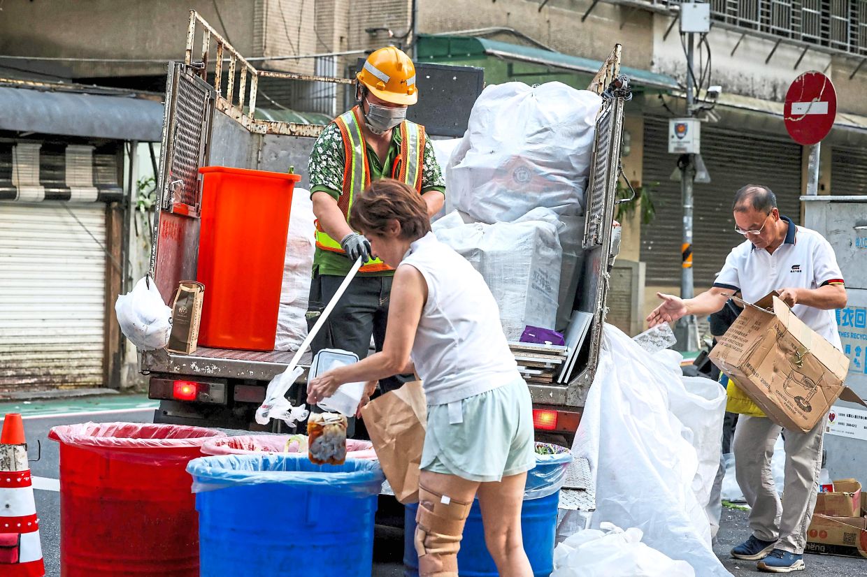A resident throwing food waste into a bucket, while another resident deposits plastic waste by the side of a recycling collection truck.