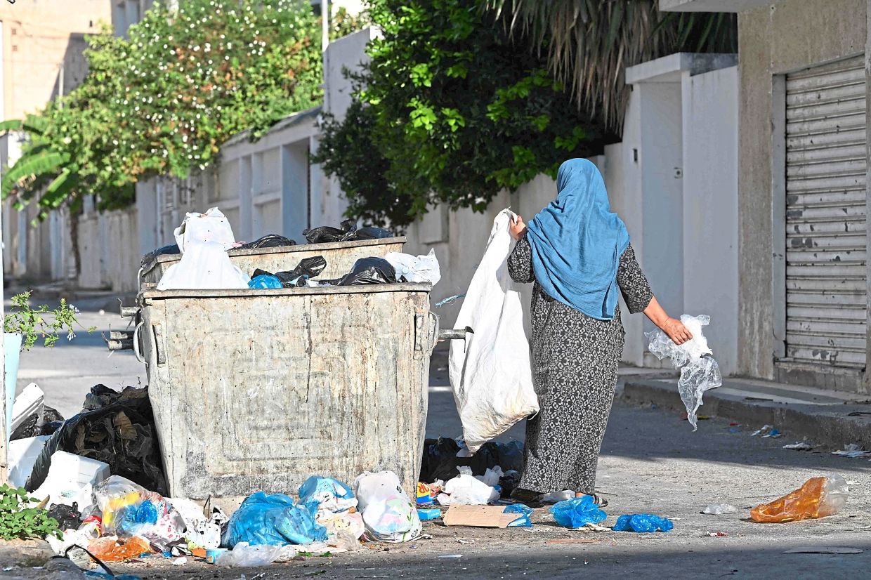 A woman ragpicker rummages through a garbage bin to salvage plastic.