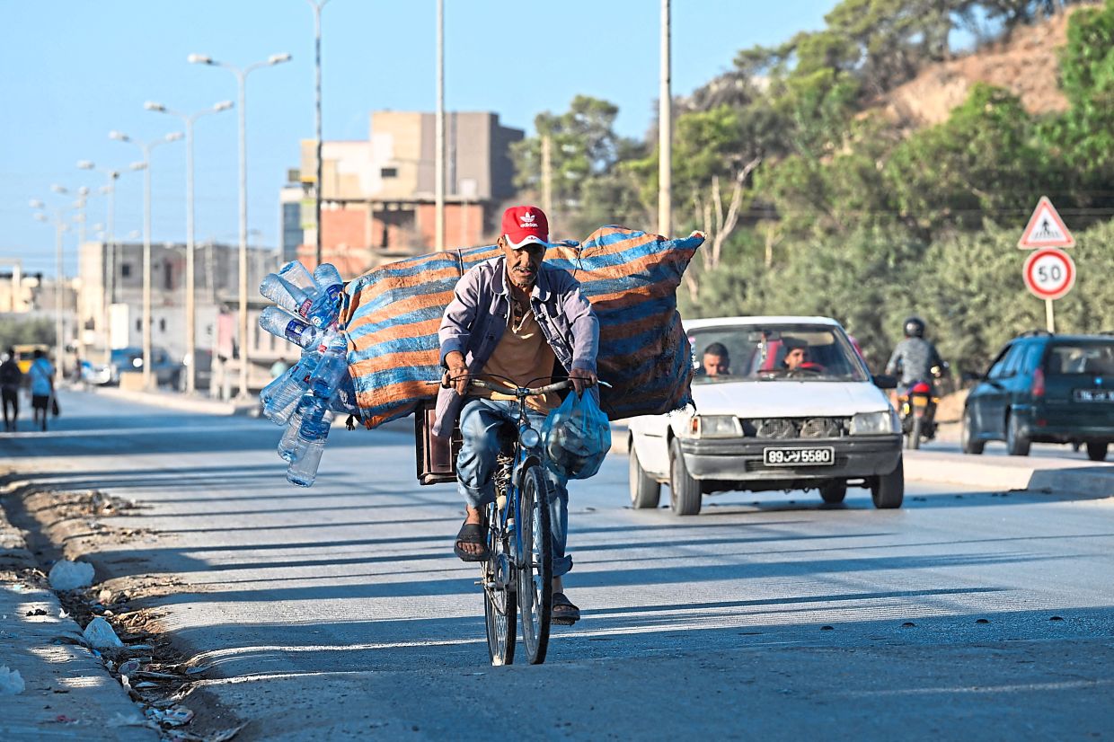 A ragpicker rides his bicycle loaded with plastic bottles salvaged from garbage containers.