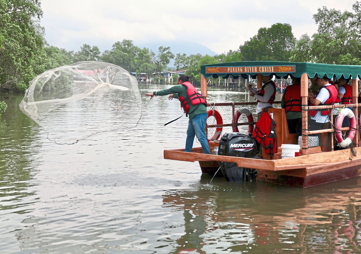 The cruise operator throwing a net to catch fish during the Penang river cruise along Sungai Juru. — ZHAFARAN NASIB/The Star.